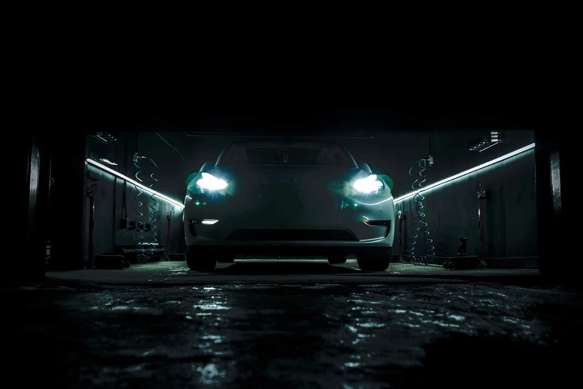 Tesla Model 3 headlights illuminating a wet floor inside the dark PitStop & Go service bay