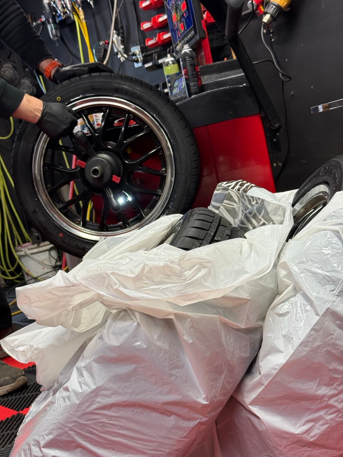 Gloved technician spinning a chrome-lipped rim on the wheel balancer during an on-rim changeover